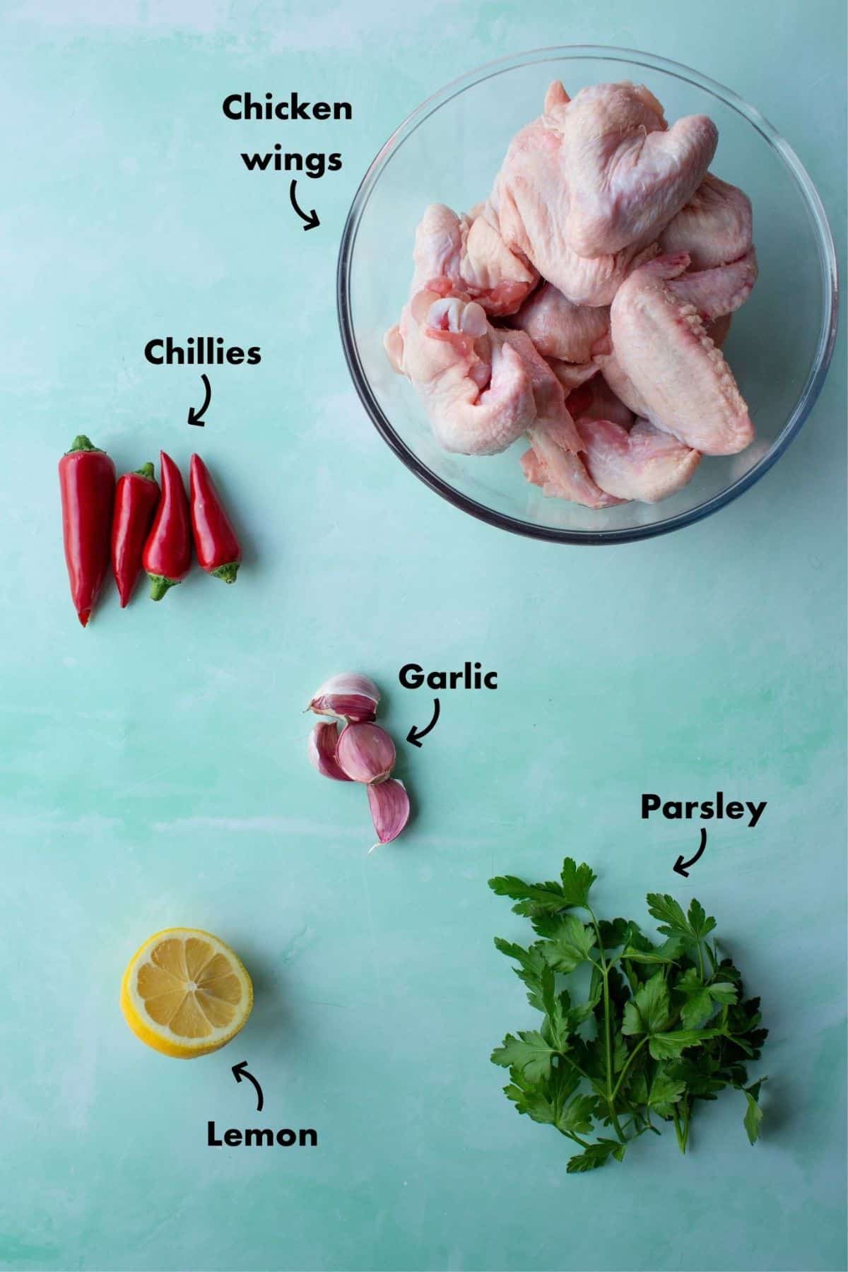 Ingredients to make the chicken wings laid out on a plae blue background and labelled.