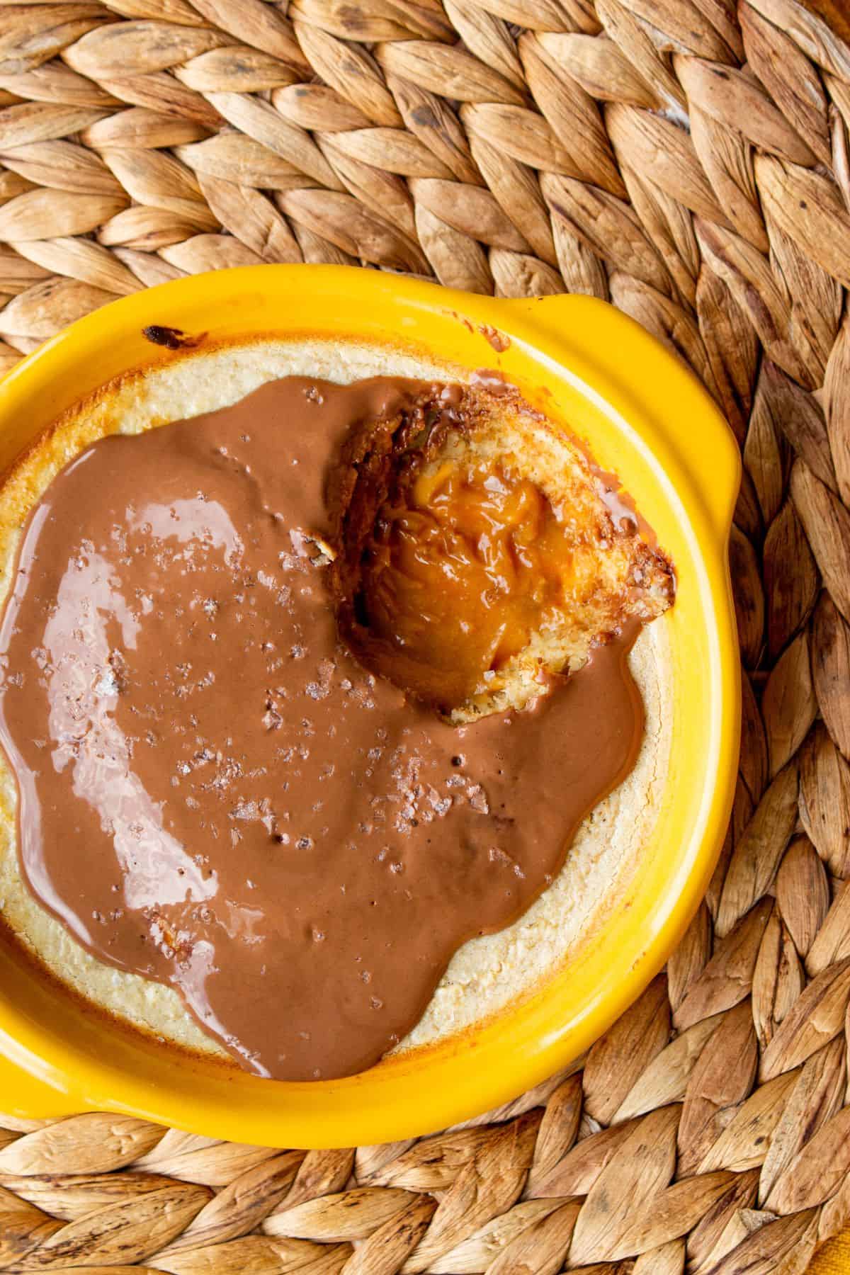 Overhead view of  Baked Oats with peanut butter with a chocolate topping in a yellow ramekin with a spoonful taken out of it on a straw heat mat.