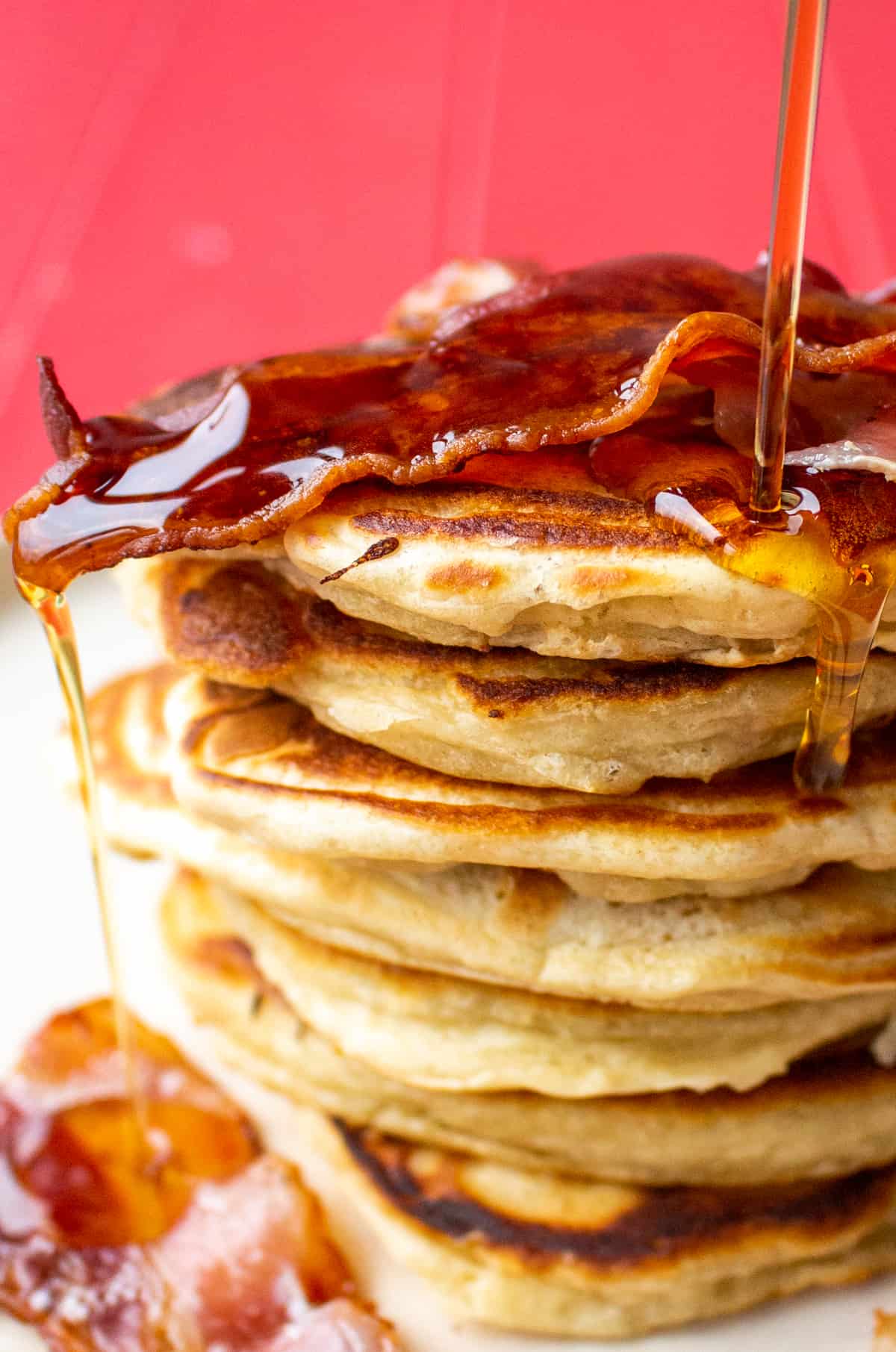 A pile of pancakes topped with crispy bacon with honey poured all over.