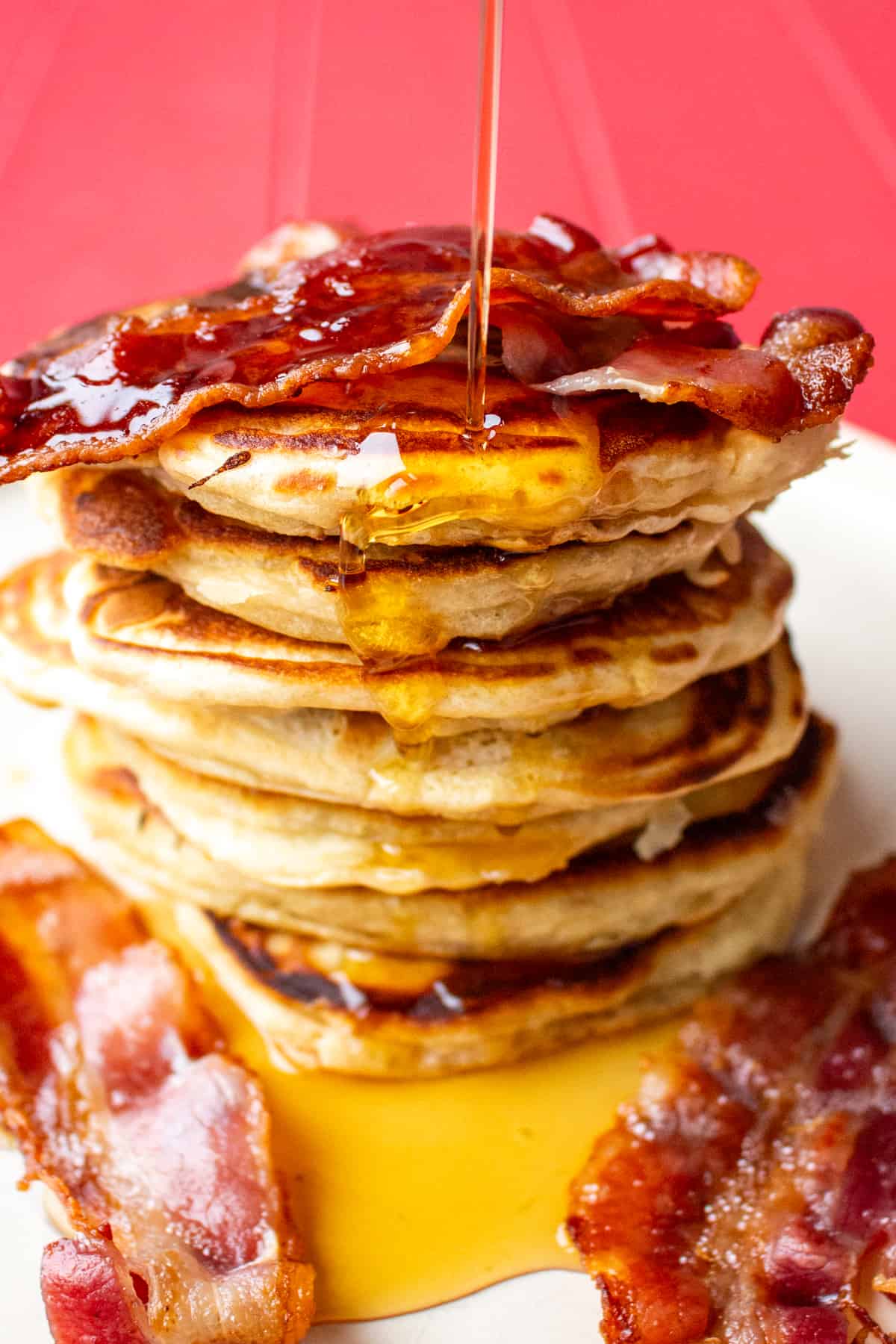 Honey being poured over a pile of pancakes topped with honey and bacon on top and on plate.
