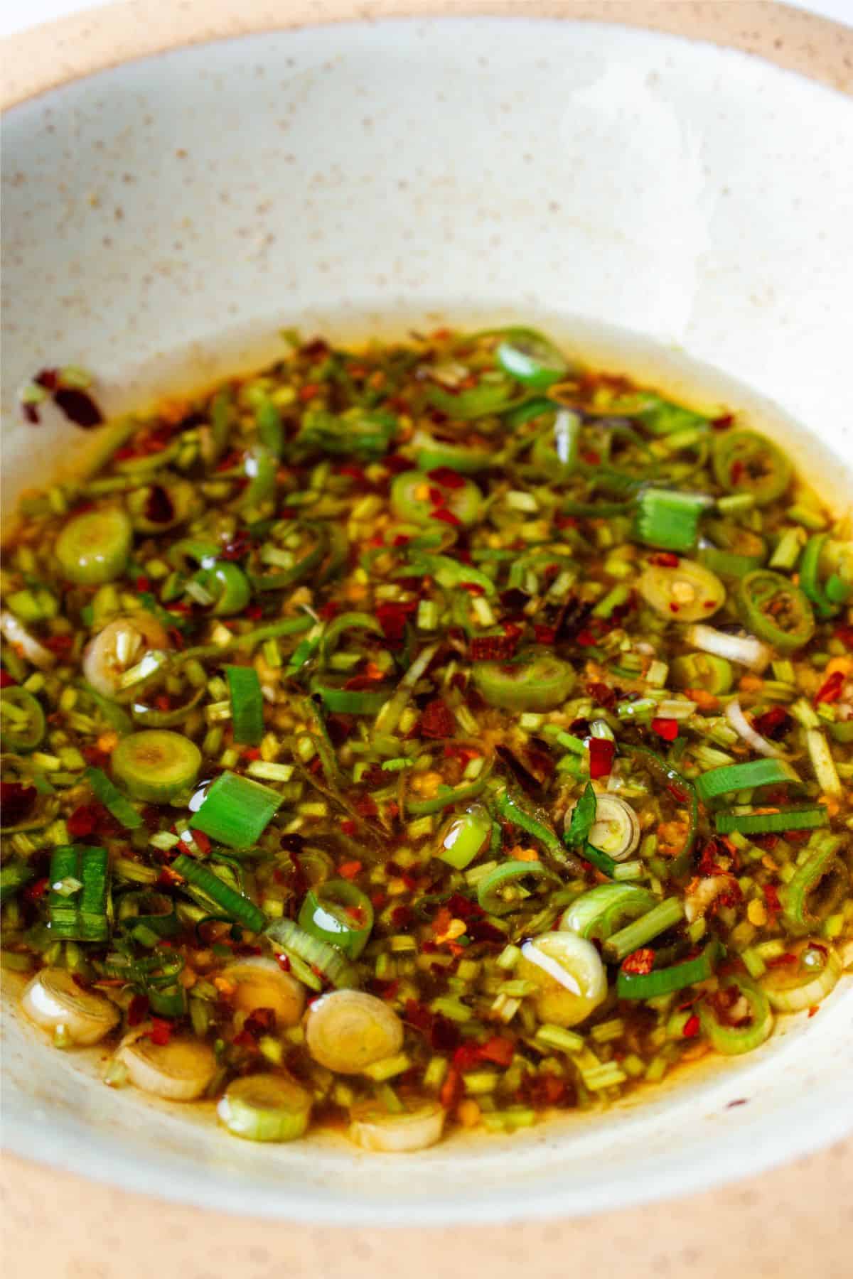 Chilli oil with sliced spring onions, chilli flakes, coriander stalks and oil in a bowl.