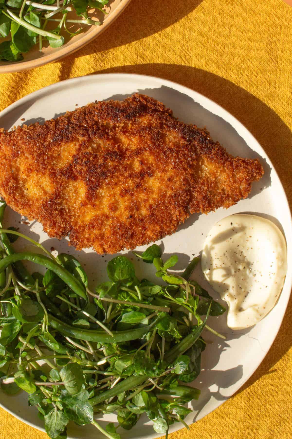Pork schnitzel on a plate with watrcress and beans and some aoili.