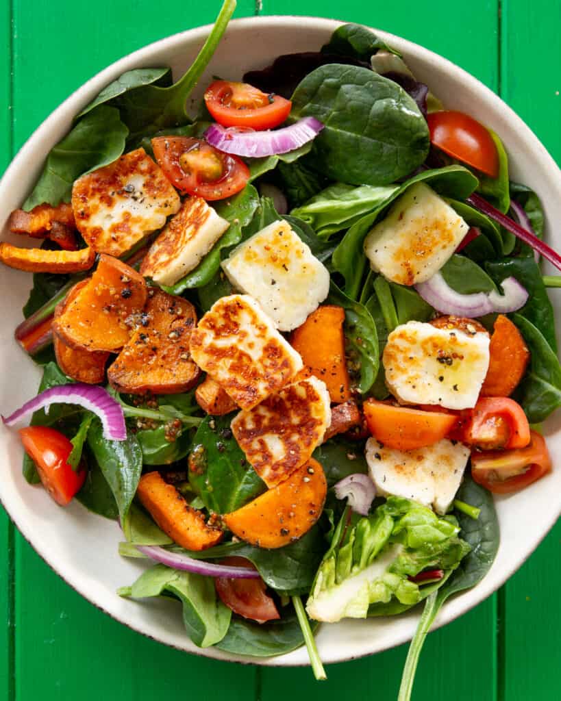 Salad in a bowl with golden browned halloumi, butternut squash, red onion and tomatoes.