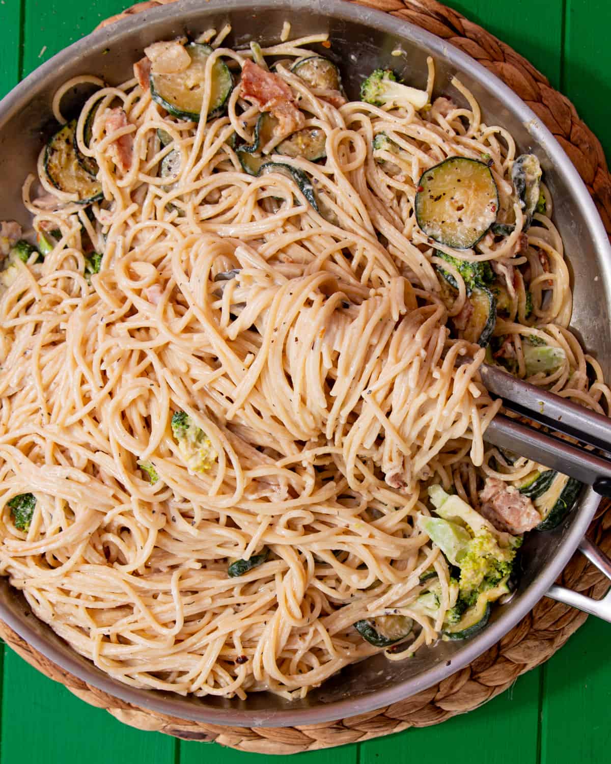 A close up of the creamy spaghetti with courgette rounds, bacon and broccoli in a large metal pan.