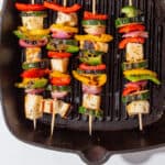 Halloumi and roasted vegetable kebabs on skewers on a griddle pan.