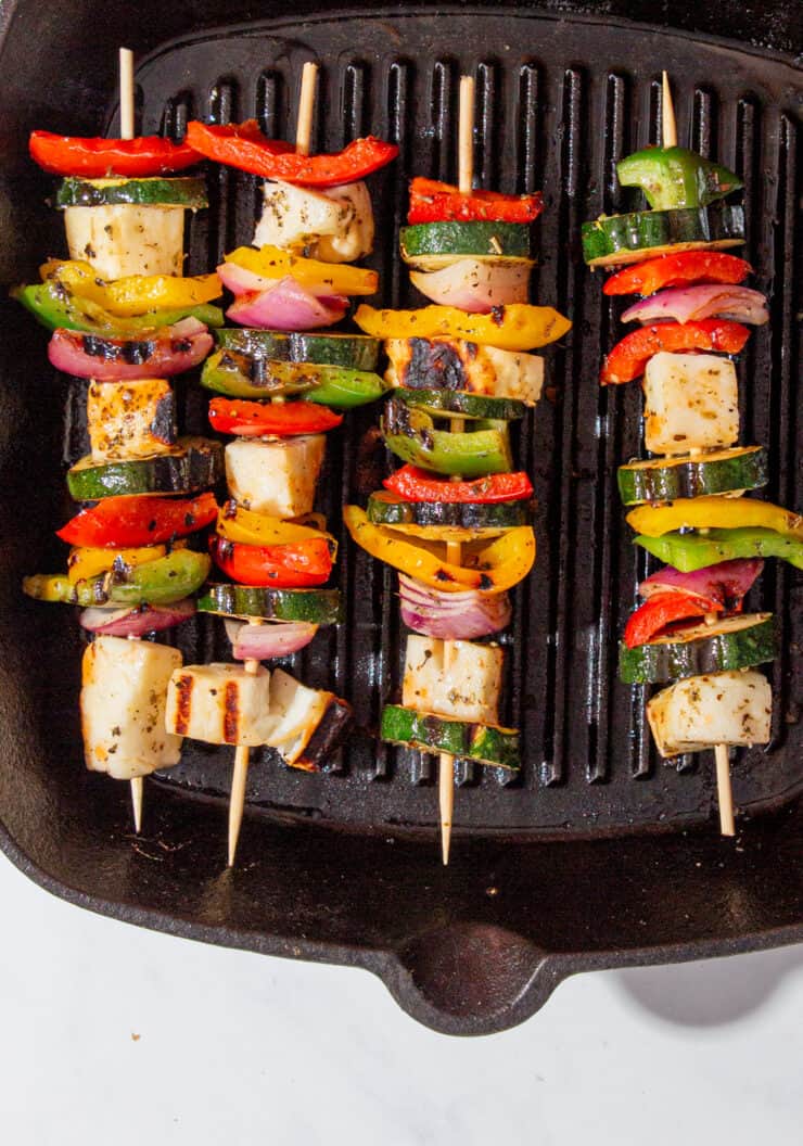 Halloumi and roasted vegetable kebabs on skewers on a griddle pan.