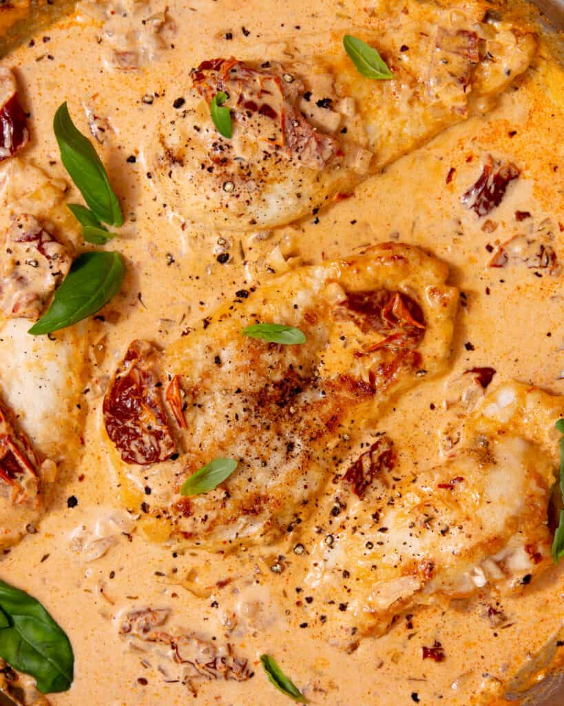 Close up of golden browned chicken pieces in a creamy tomatoey sauce topped with fresh basil.