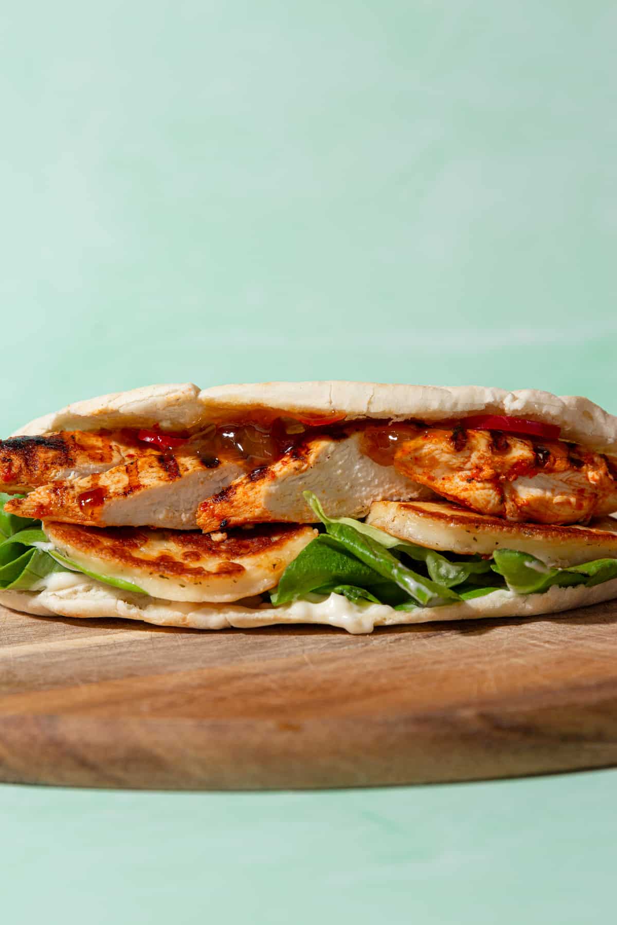 Side view of pitta filled with browned halloumi, lettuce, chicken, mayo and relish.