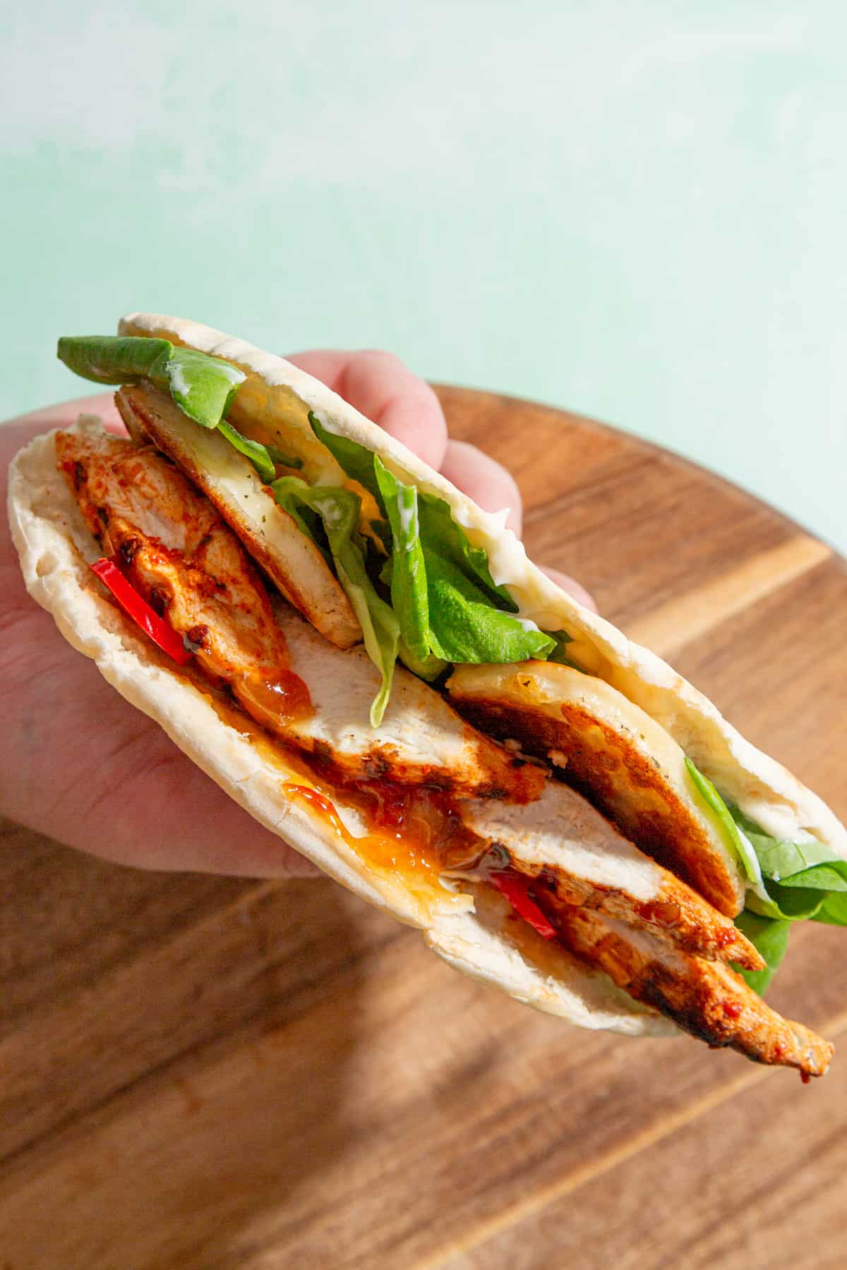 Side view of pitta being held in one hand and filled with browned halloumi, lettuce, chicken, mayo and relish.