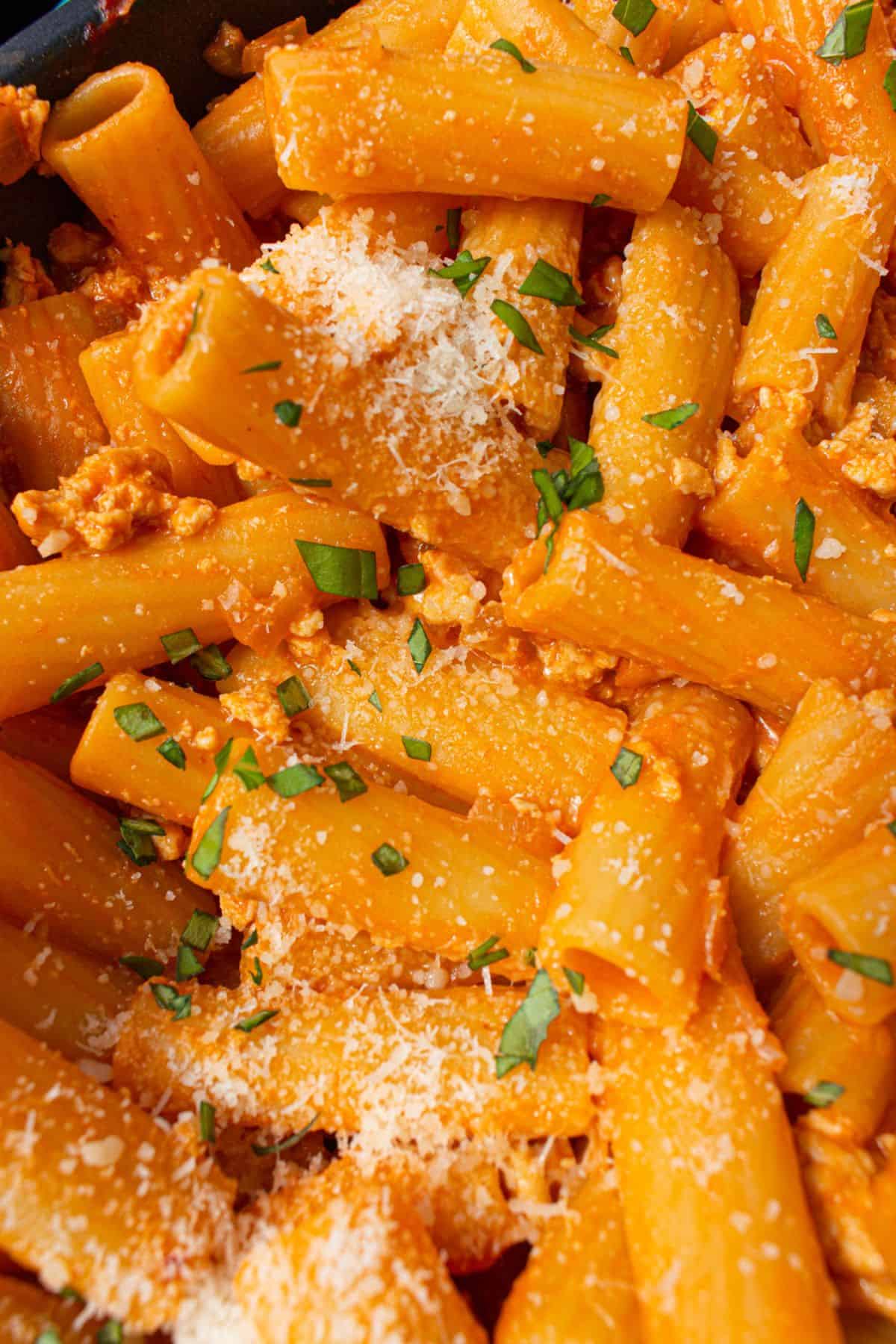 close up of rigatoni pasta with sauce topped with grated parmesan cheese and chopped basil.