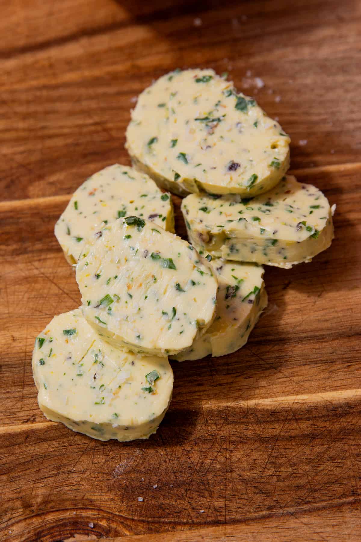 Rouns aof herby butter piled on each other on a wooden chopping board.