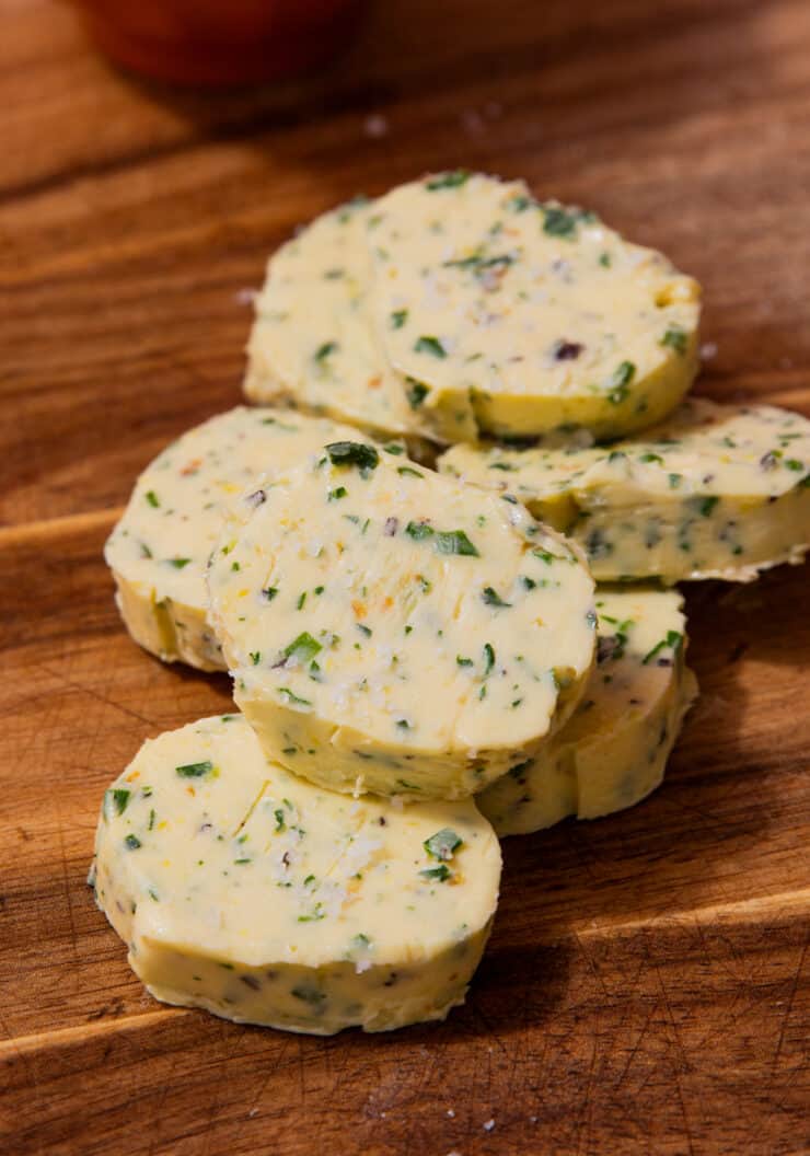5 round pieces of butter with herbs piled on top of each other on a wooden board