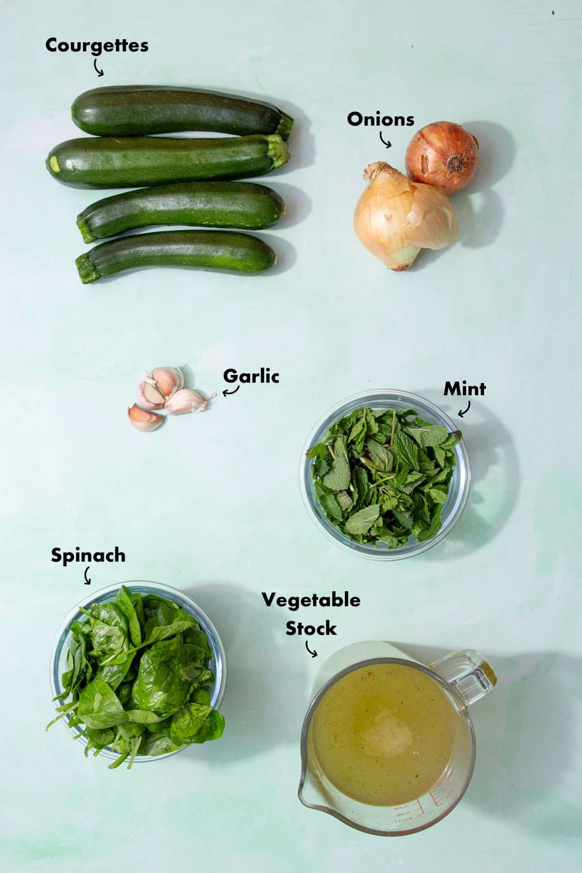 Ingredients to make courgette soup laid out on a pale blue background and labelled.