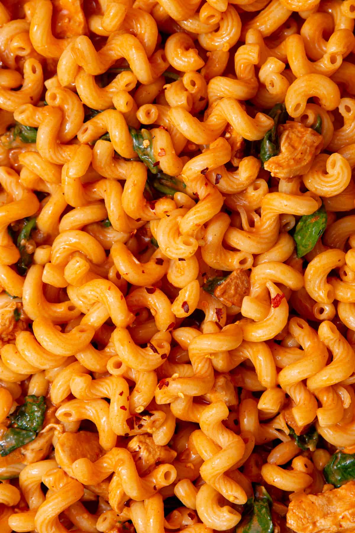 Close up of spirali pasta with bits of chorizo covered in a tomatoey sauce, with some wilted spinach and topped with some grated cheese.