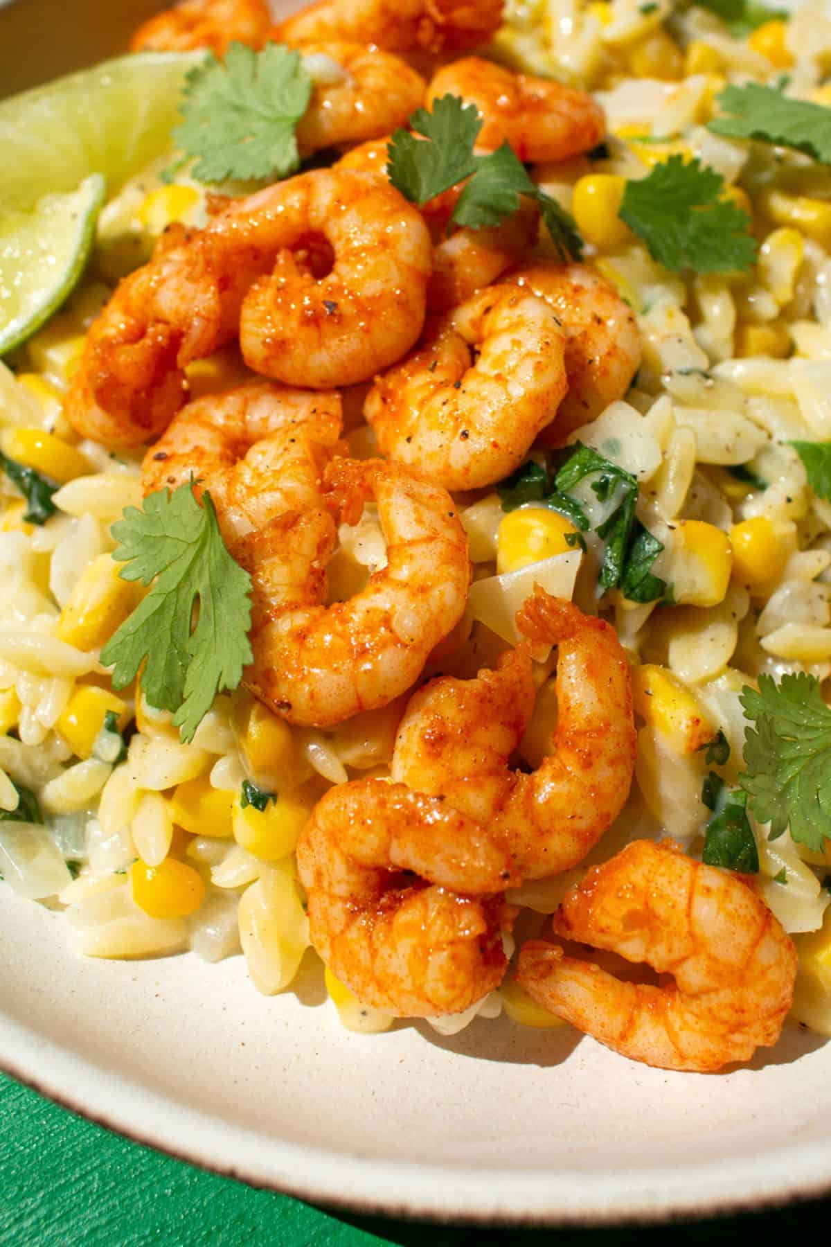 Close up of orzo, sweet corn, spicy prawns topped with lime wedges and coriander.
