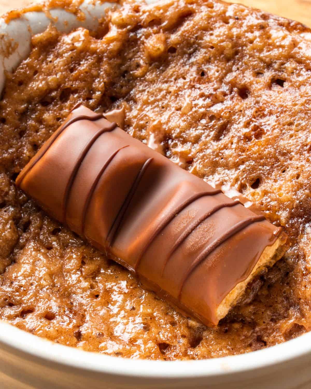 Close up of a mug cake with a piece of chocolate bar over the baked cake mix in a white ramekin. 