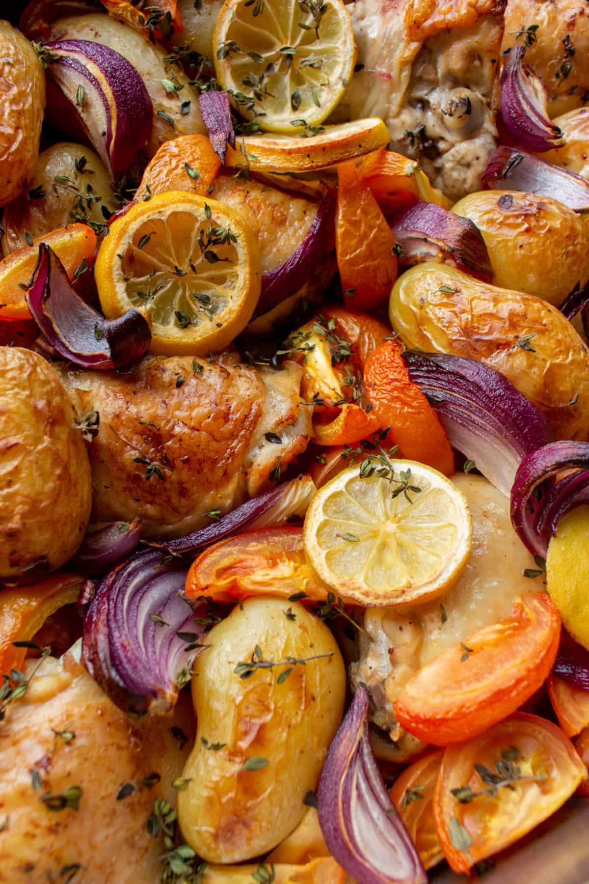 Close up shot of golden browned chicken thighs, new potatoes and vegetables all baked with lemon rounds and red onions.