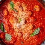 Meatballs in tomato sauce in a large pan topped with grated cheese and fresh basil leaves.
