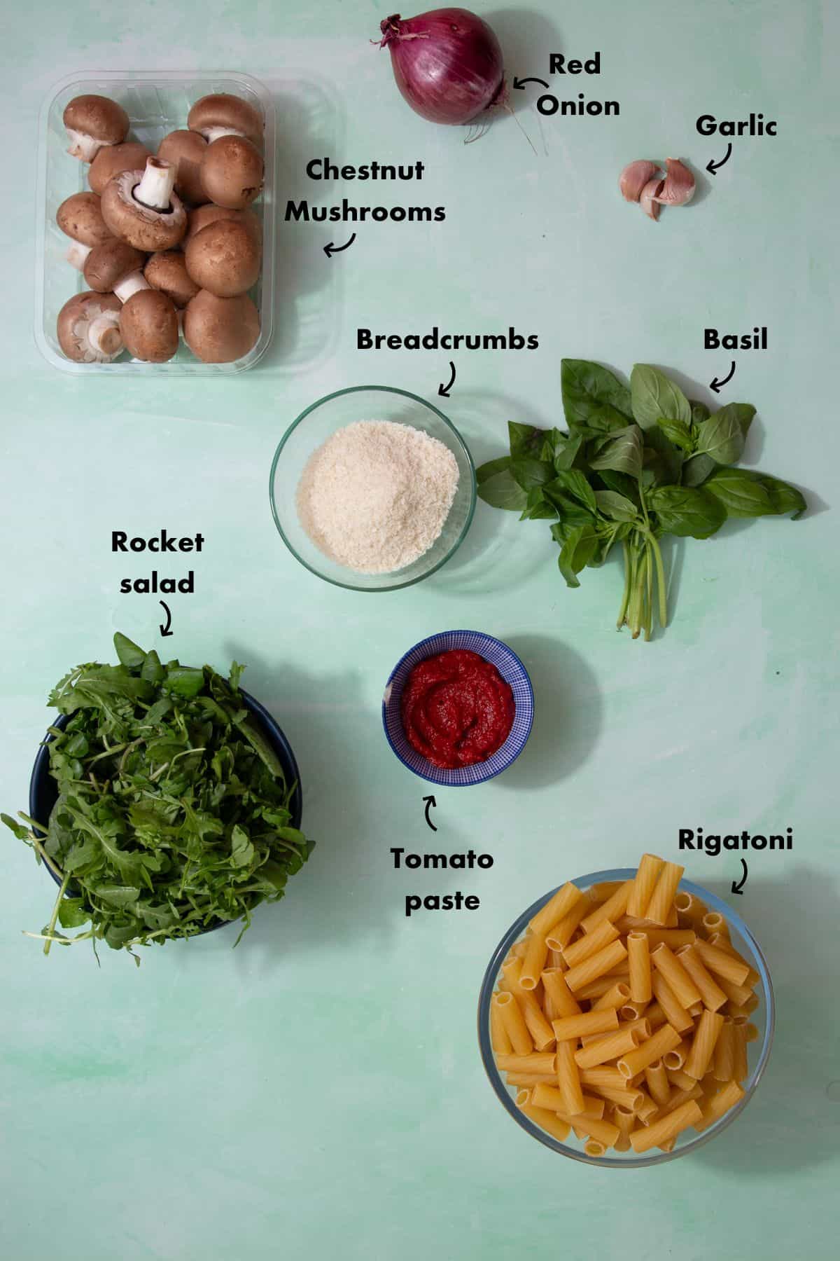 Ingredients to make mushrooms with rigatoni laid out on a pale blue background and labelled.