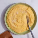 A green bowl of polenta with parmesan sprinkled over with a spoon.
