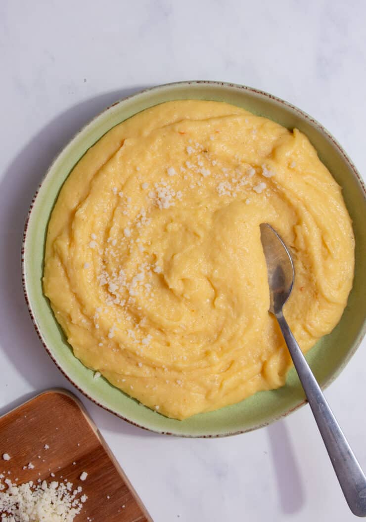 A green bowl of polenta with parmesan sprinkled over with a spoon.