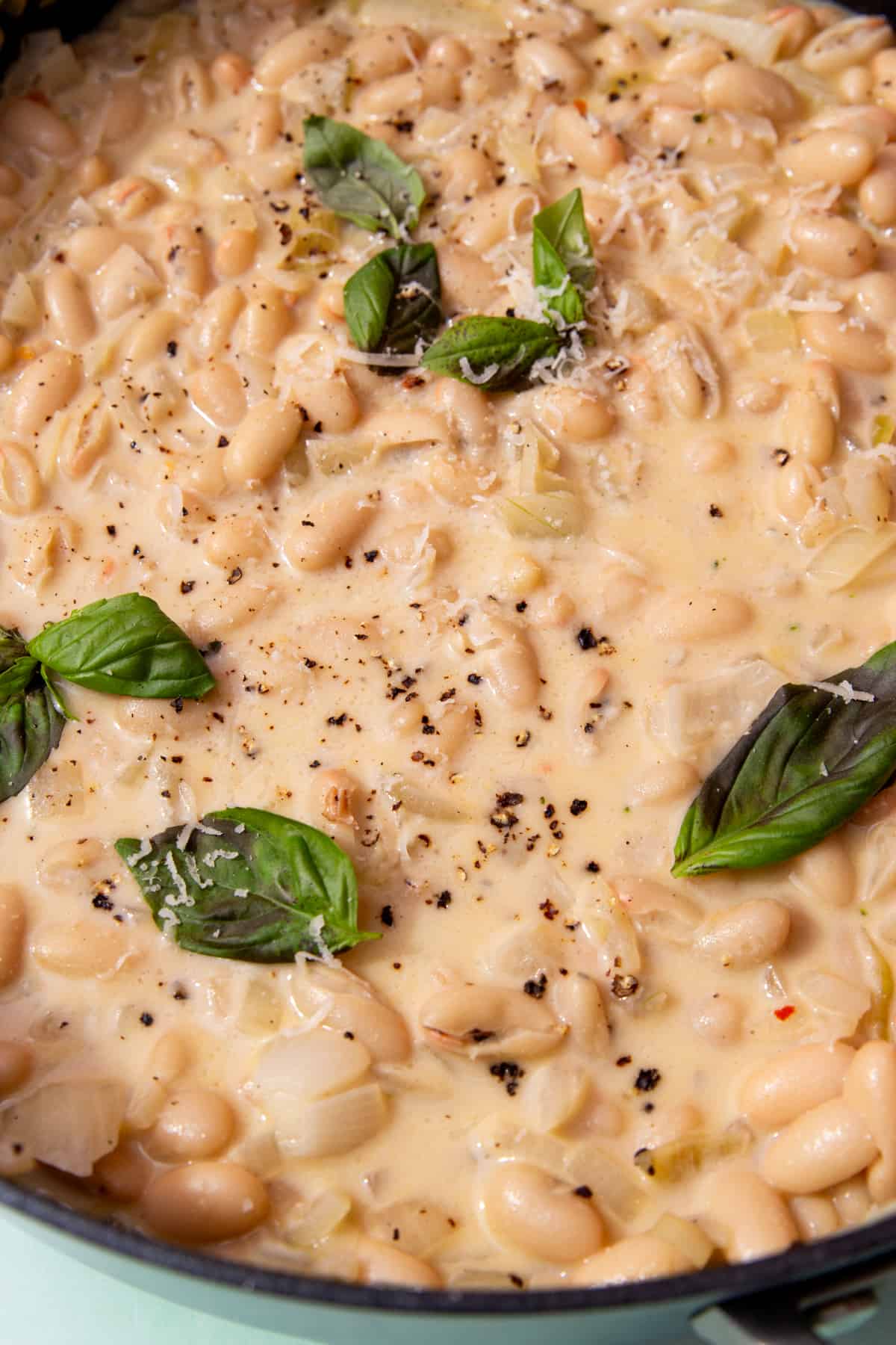 Close up of creamy cannellini beans in a sauce topped with fresh basil leaves, grated cheese and chilli flakes.