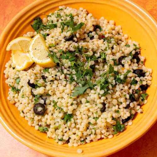 couscous served in a yellow bowl, topped with lemon wedges and parsley