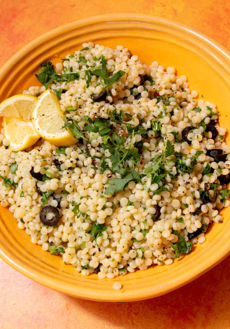 couscous served in a yellow bowl, topped with lemon wedges and parsley