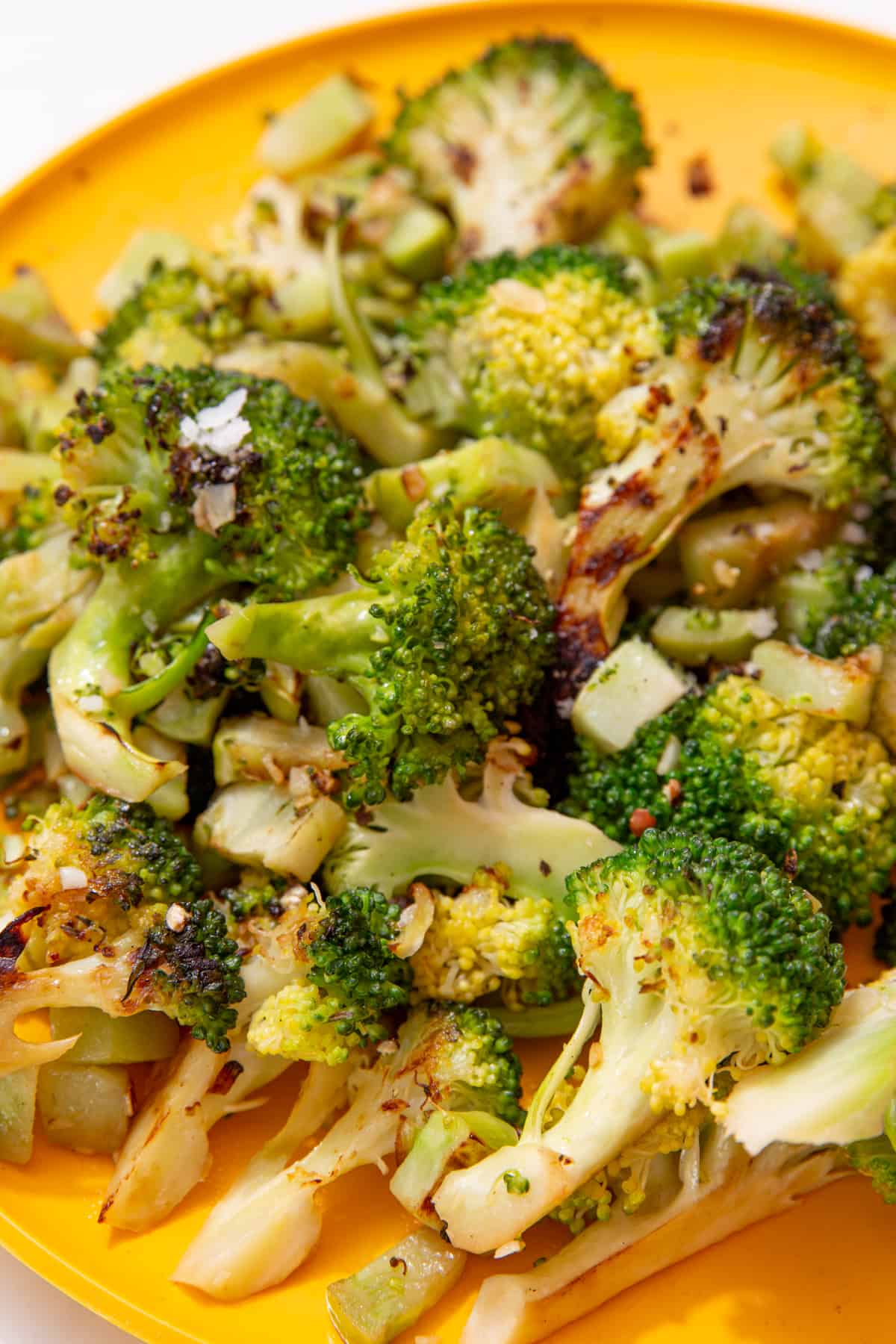 A close up shot of florets of cooked and charred broccoli on a yellow plate. 