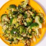 A yellow plate full of browned and cooked broccoli florets.