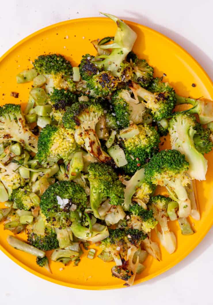 A yellow plate full of browned and cooked broccoli florets.