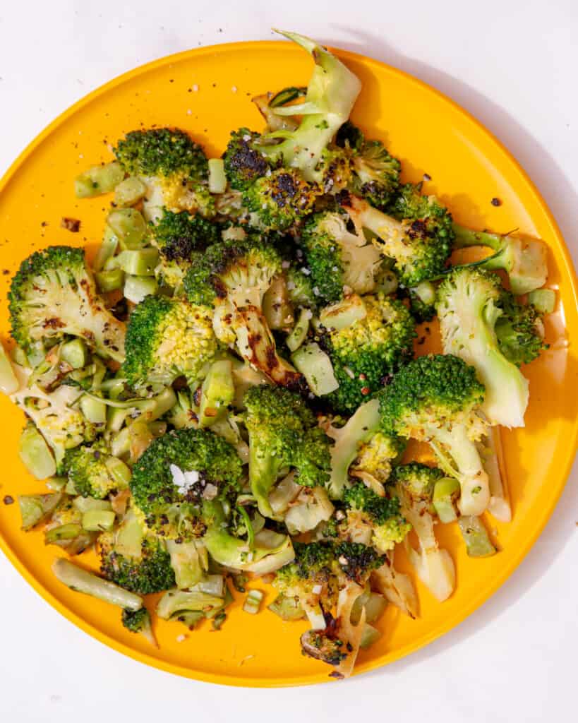 A yellow plate full of browned and cooked broccoli florets.
