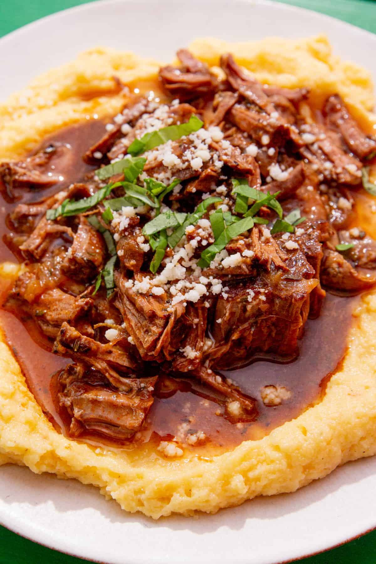 A close up of shredded steak with gravy served over a bed of polenta.