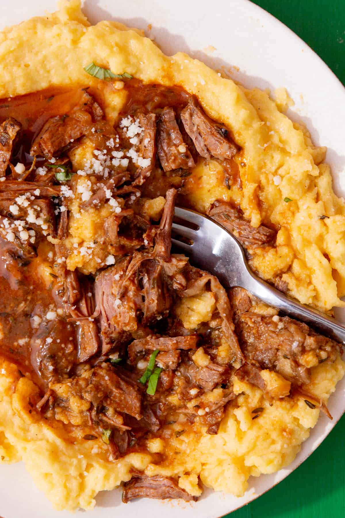 A close up of shredded steak with gravy served over a bed of polenta with a fork on the plate.