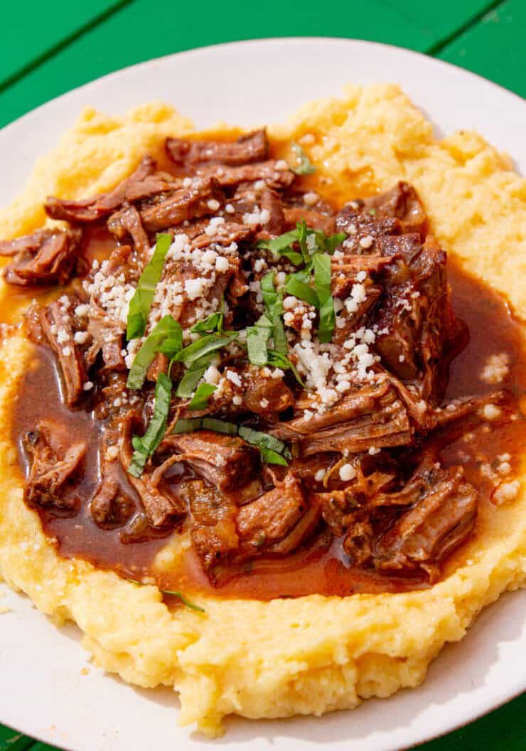 A plate with shredded steak and gravy over a bed of polenta.