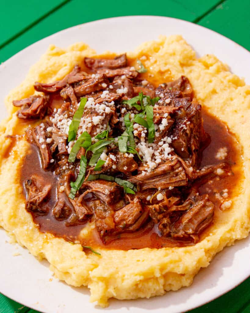 A plate with shreeded steak and gravy over a bed of polenta.