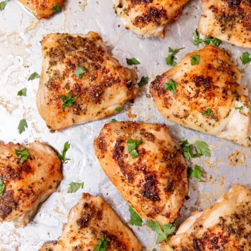 Chicken thighs on a silver baking tray topped with parsley