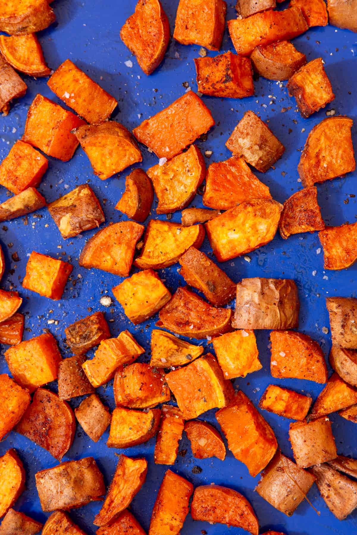 roasted sweet potato cubes with some coarse salt displayed on a blue tray.