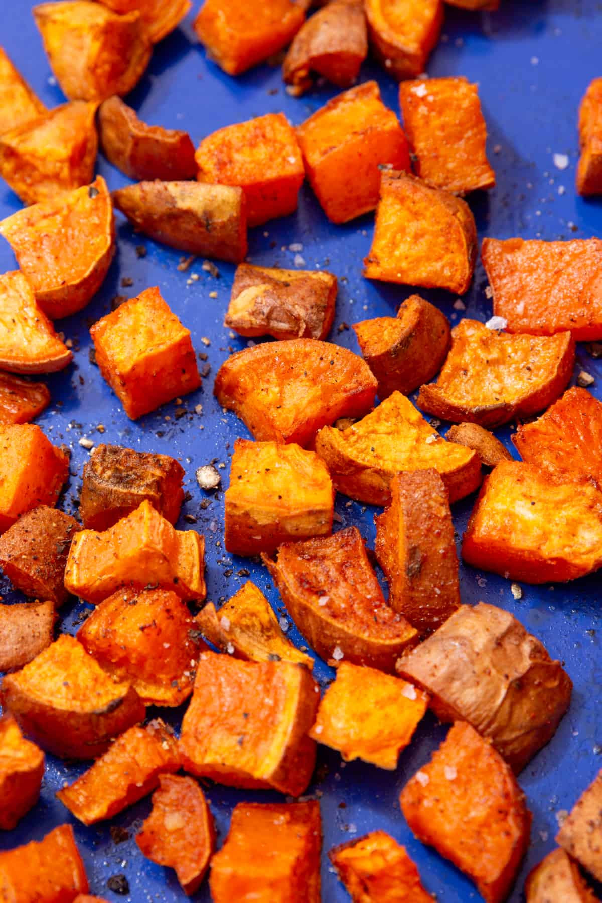 roasted sweet potato cubes spread out on a blue tray topped with some coarse salt.