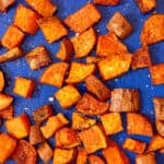 Roasted sweet potatoes cube spead out over a blue tray.