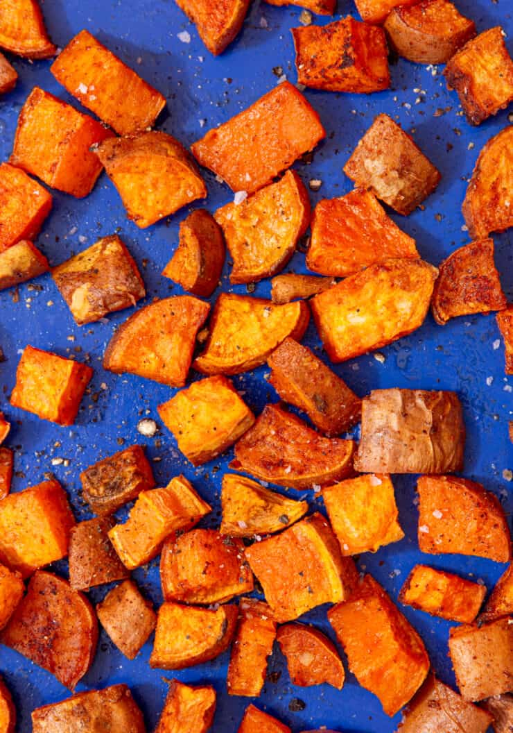 Roasted sweet potatoes cube spead out over a blue tray.