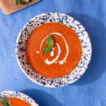 Two bowls of soup and one chopping board with basil on.