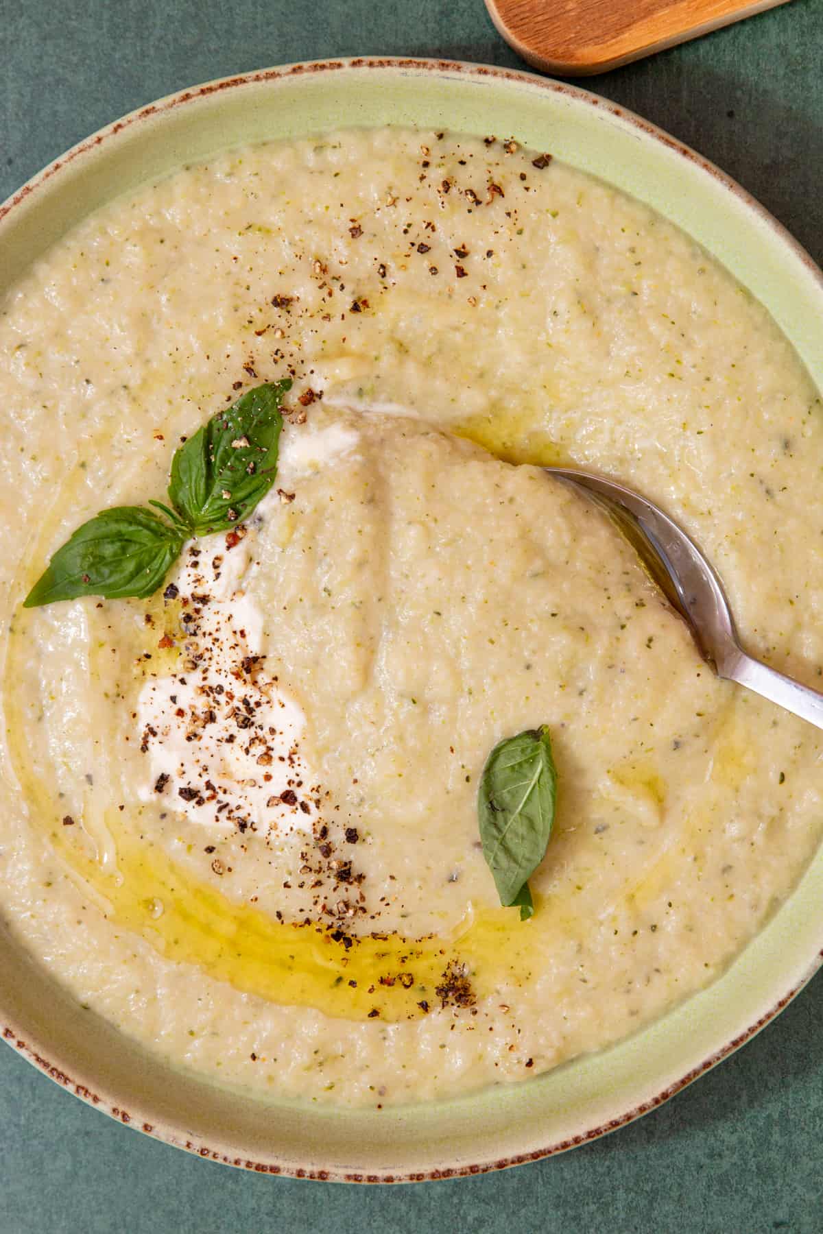 A bowl with a thick, creamy soup and a swirl of oil and cream topped with fresh basil and chilli flakes.