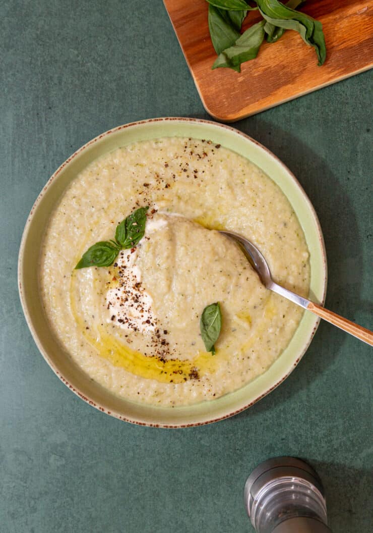 A bowl of thick, creamy soup topped with drizzle of oil, cream and fresh basil.