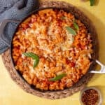 A large pan with baked pasta topped with golden browned cheese and fresh basil.