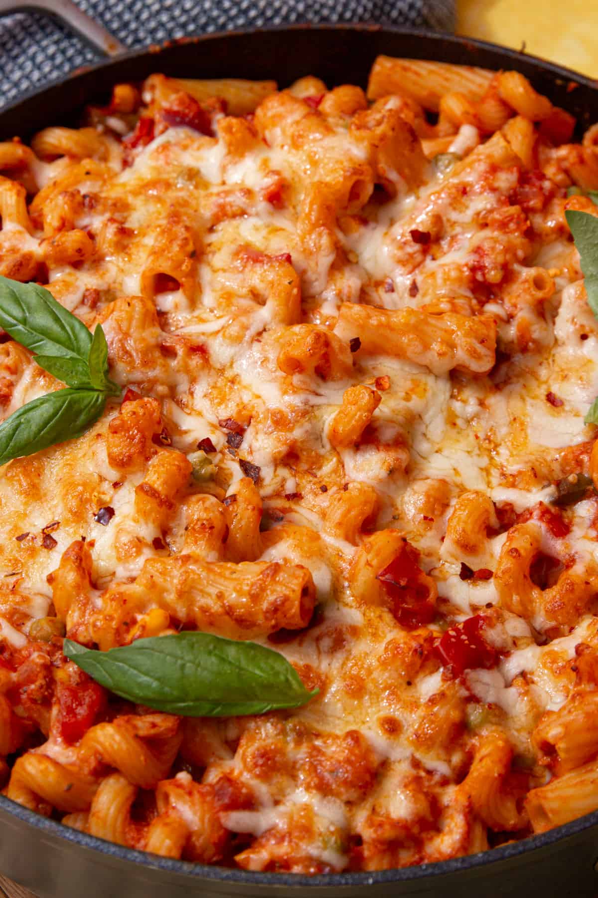 Close up of tuna and tomato pasta bake topped with melted cheese and fresh basil in a pan. 
