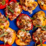 Baked red and yellow pepper halves with rice and sausage filling on a blue tray.