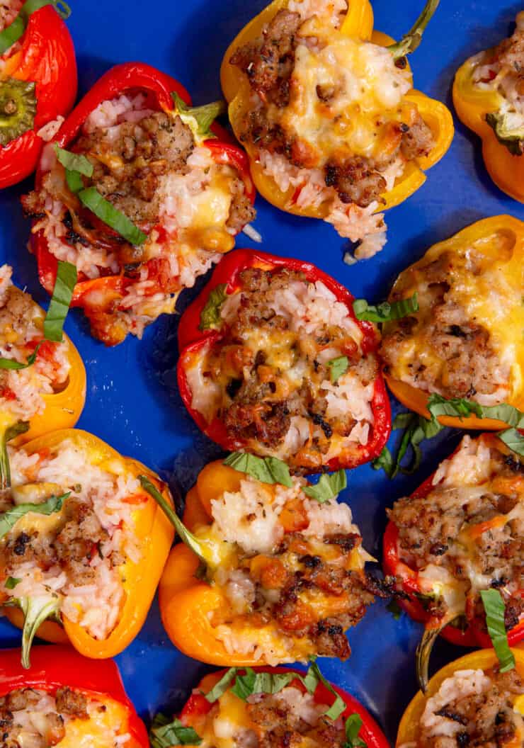 Baked red and yellow pepper halves with rice and sausage filling on a blue tray.