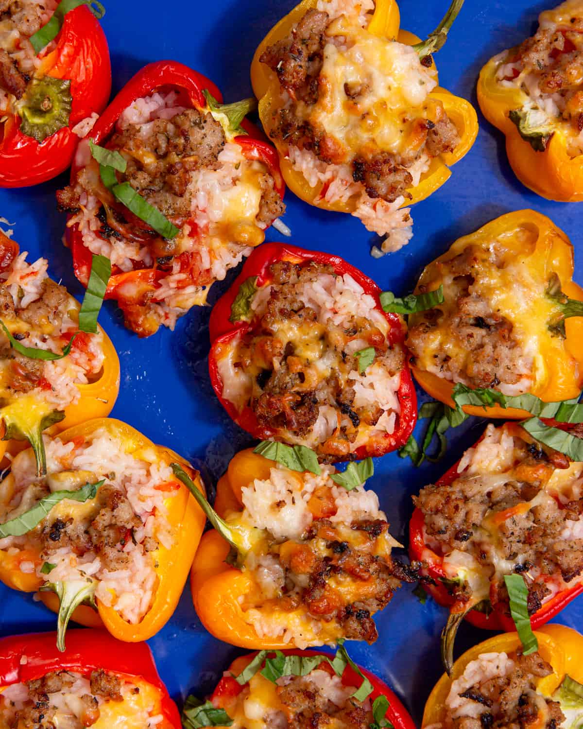 Baked red and yellow pepper halves with rice and sausage filling on a blue tray.