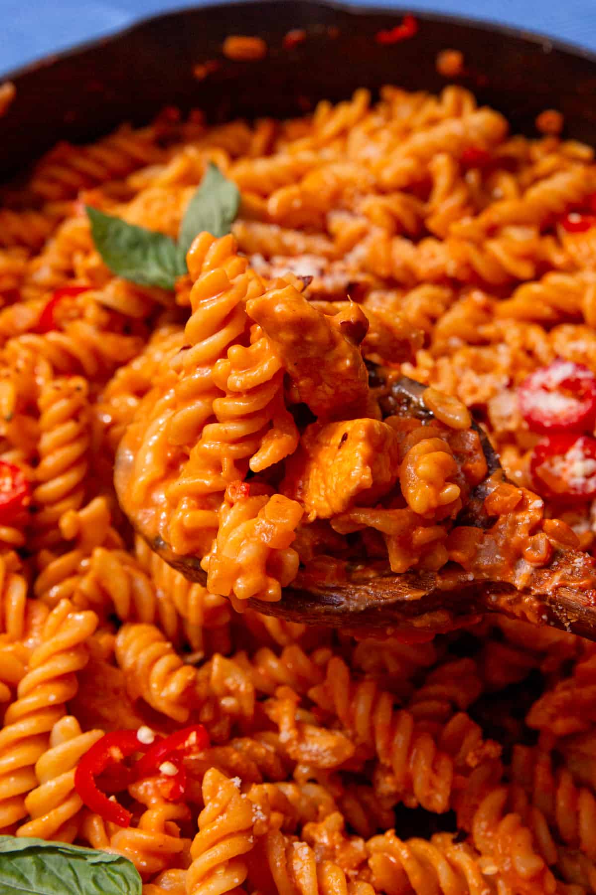 Tomatoey, saucy fusilli pasta with chicken in a pan mixed with a wooden spoon and topped with fresh basil.